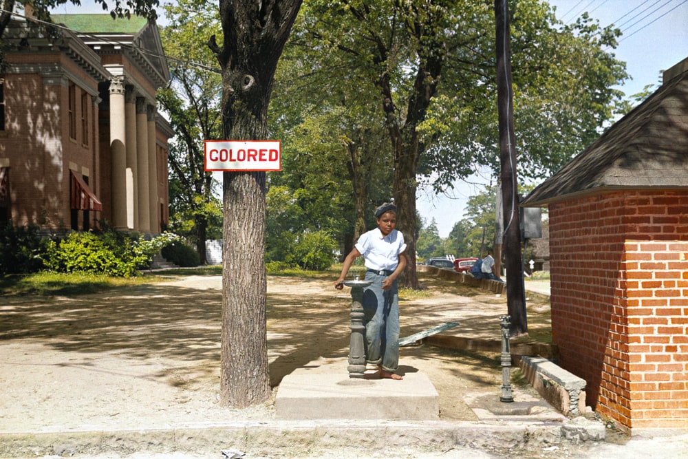 An African American Child Standing Between a Drinking Fountain and Tree Labeled ‘Colored,’ Alluding to the Segregation that Sparked the Civil Rights Movement